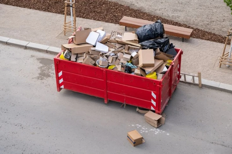 Red dumpster overflowing with cardboard boxes and packing materials on a concrete sidewalk. open top dumpster rental plano