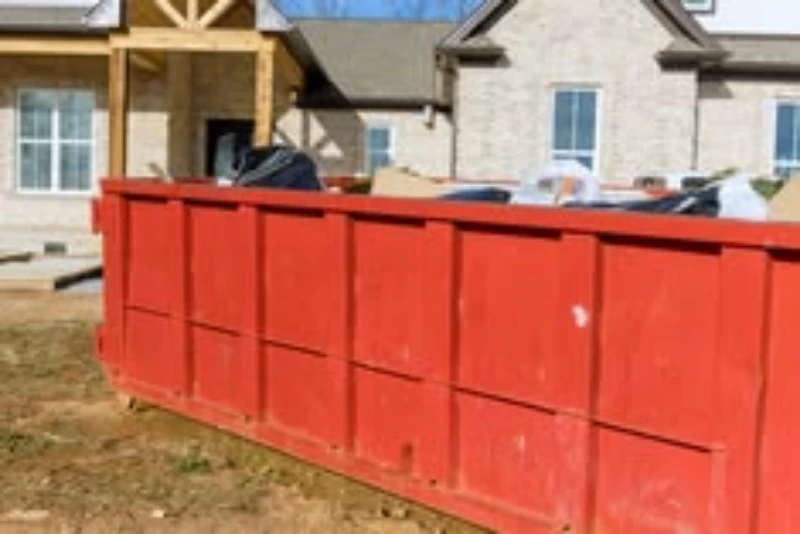 A large red dumpster in front of a house under construction.