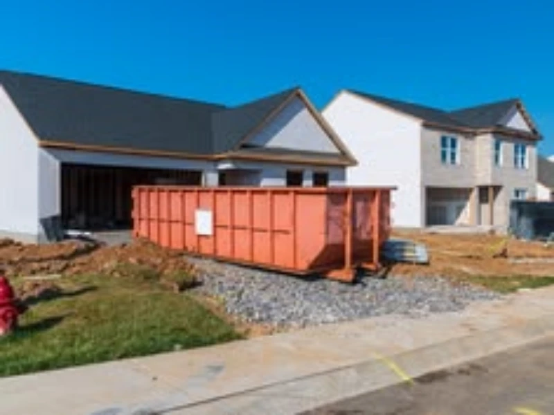 A construction site with two houses under development and a large orange dumpster in the foreground.