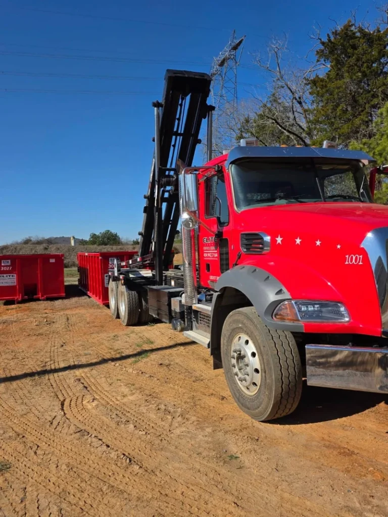 A red truck with a crane is parked next to red dumpsters on a dirt lot under a clear blue sky.

A red truck with a crane is parked next to red dumpsters on a dirt lot under a clear blue sky.