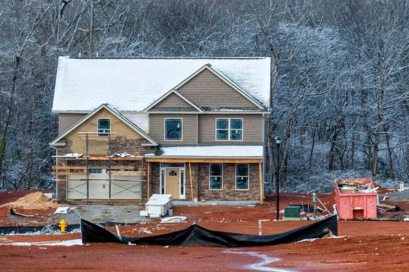 A partially constructed house in a snowy landscape, with construction materials and equipment visible around the site.