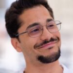 Portrait of a confident man with glasses and a beard, smiling outdoors.