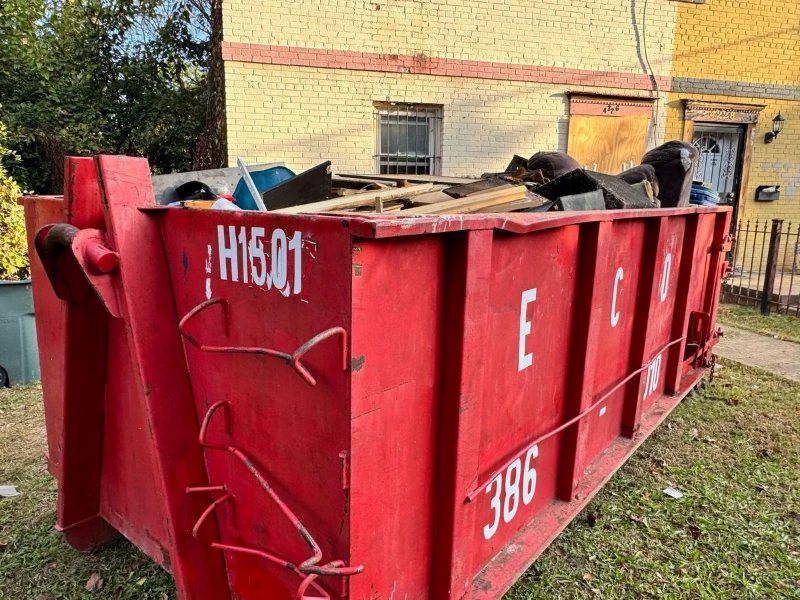 Red construction dumpster labeled “H5E01” and “386” overflows with debris beside a weathered yellow brick building on a sunny day. Dumpster Rental Allen