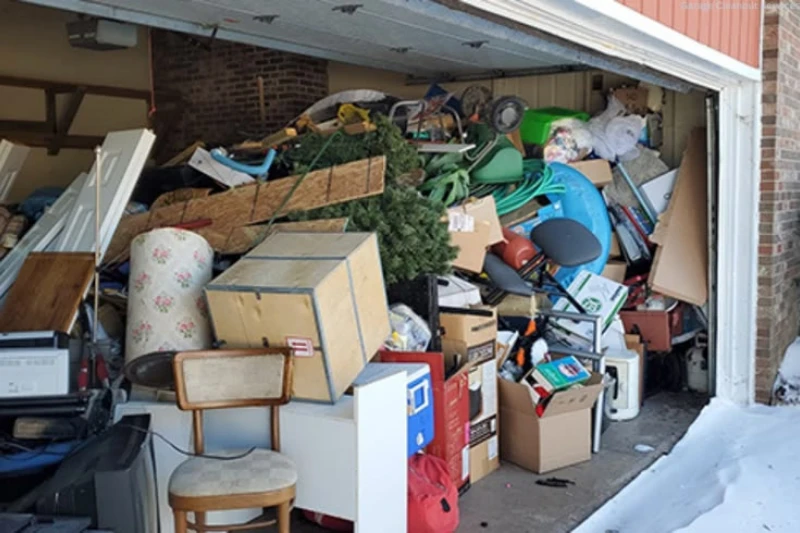 Open garage overflowing with boxes, furniture, bicycles, tools, and holiday items, creating a cluttered, crowded scene beside a snowy driveway.