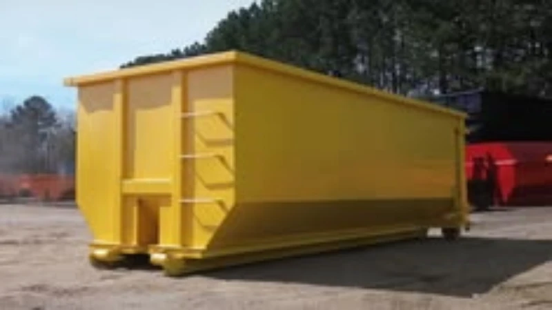 Large yellow industrial dumpster sits outdoors on pavement, with a ladder at its front, trees behind, and a red container nearby; utilitarian scene.